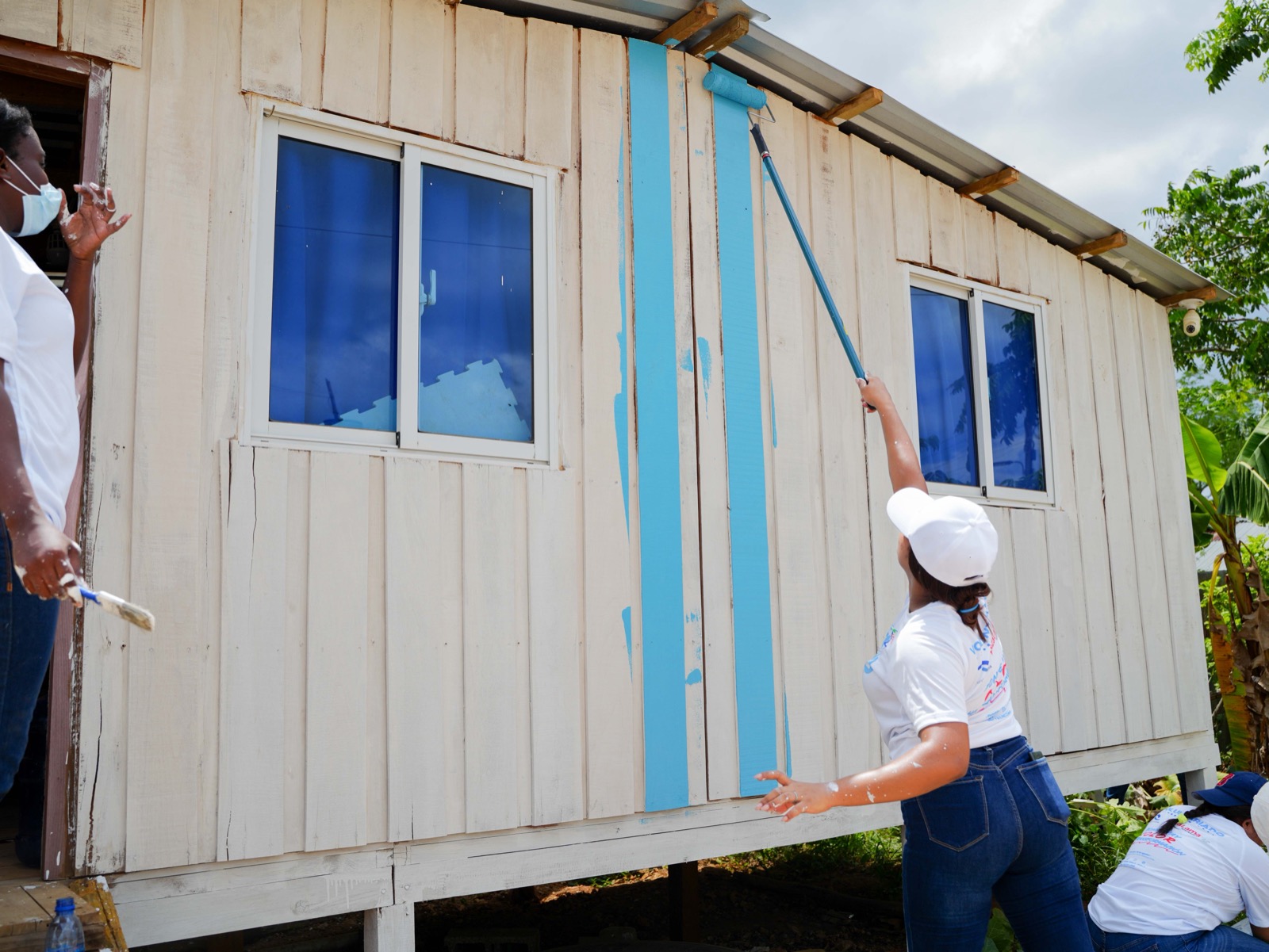 Voluntaria de Plaza Lama pasando el rodillo con pintura azul sobre una vivienda de madera